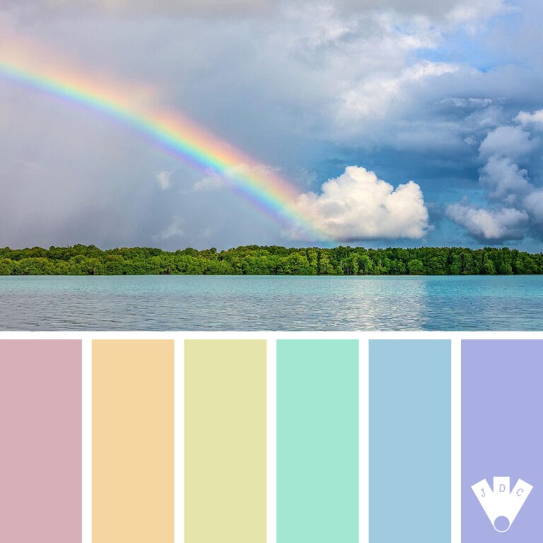 Arc-en-ciel pastel au-dessus d’un lac turquoise et d’une forêt sous un ciel nuageux.